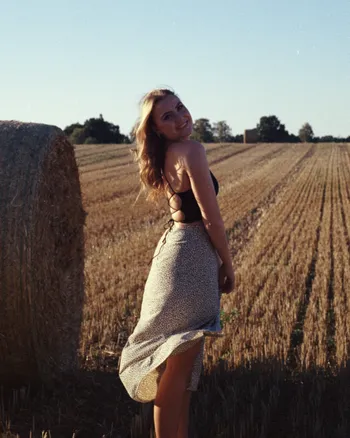 Frau im sommerlichen Outfit tanzend auf dem Feld zum Sonnenuntergang